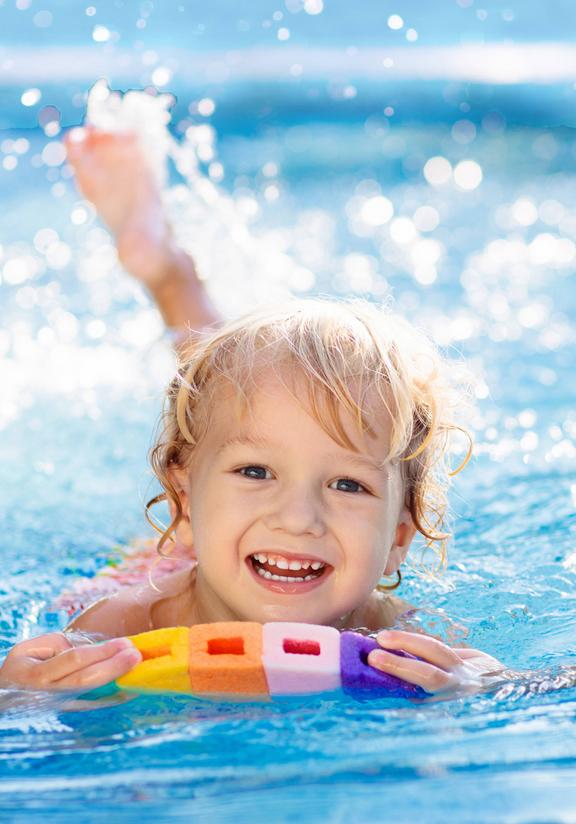 Kind im Schwimmbecken mit buntem Schwimmbrett, das beim Schwimmenlernen hilft.