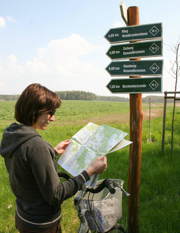 Eine Frau mit Radkarte vor einem Wegweiser in der Dübener Heide 