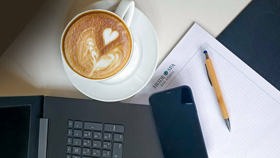 Laptop und Handy im Tagungsraum mit Tasse Kaffee und Schreibutensilien